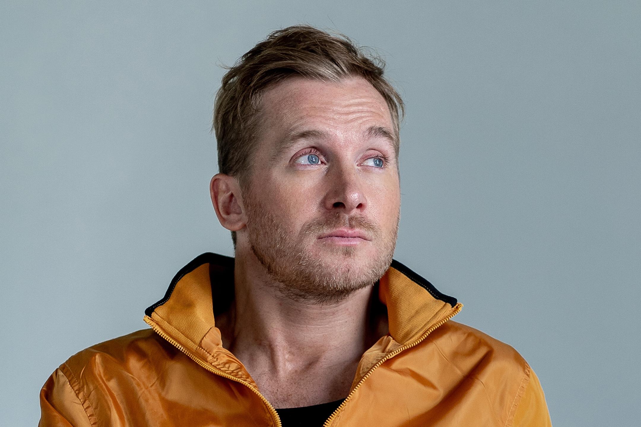 ein Mann vor einem grauen Hintergrund mit einer gelben Jacke