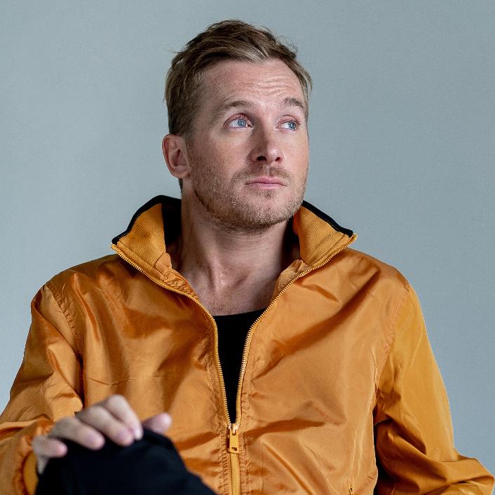 ein Mann vor einem grauen Hintergrund mit einer gelben Jacke