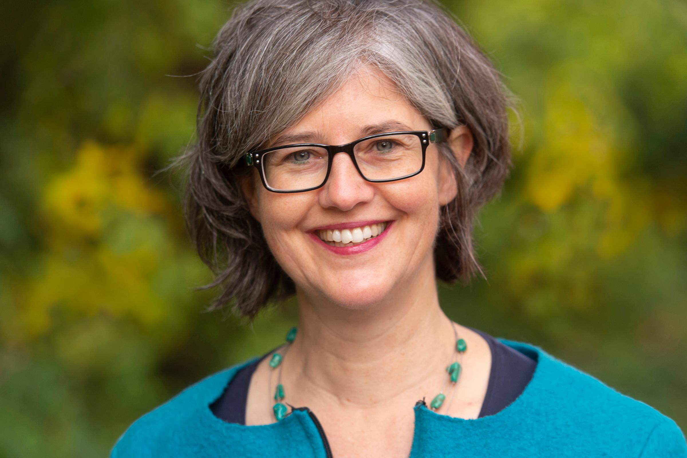 eine Frau mit einem türkisen Oberteil vor einem grün verschwommenen Hintergrund