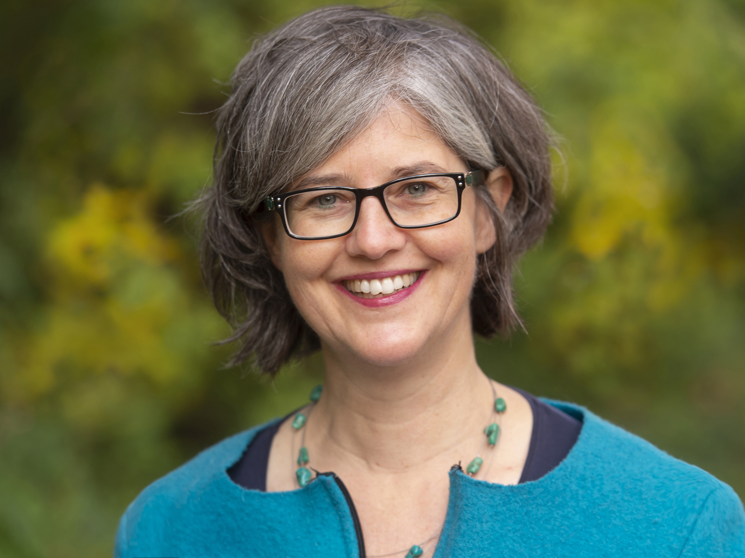 eine Frau mit einem türkisen Oberteil vor einem grün verschwommenen Hintergrund