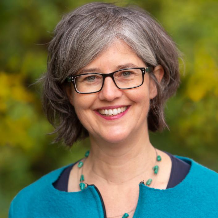 eine Frau mit einem türkisen Oberteil vor einem grün verschwommenen Hintergrund