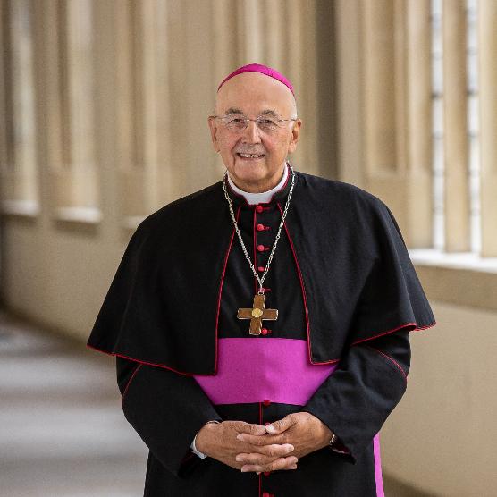 ein Bischof steht in einem Gang welcher beige Mauern hat