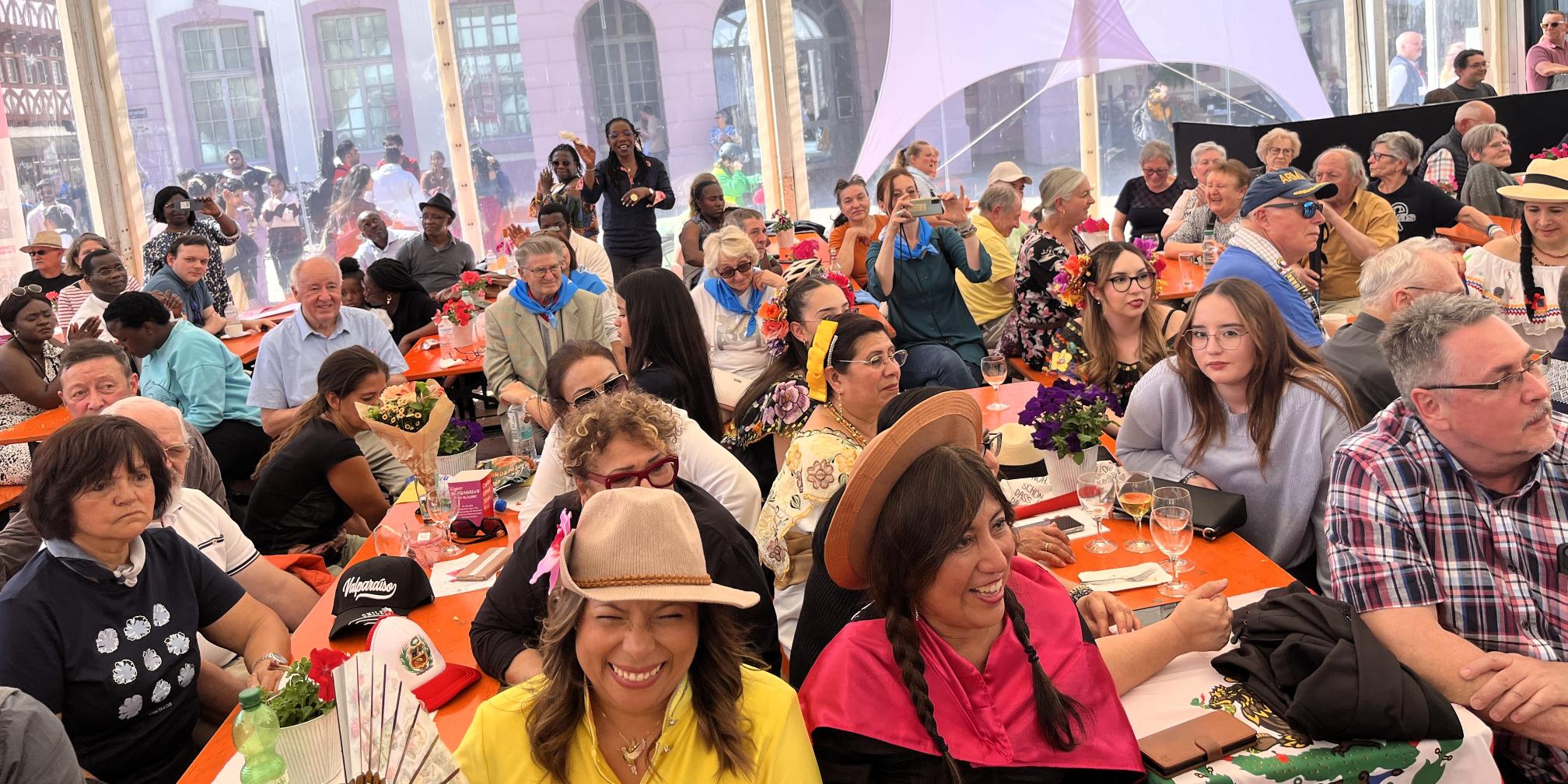 viele bunt gekleidete Menschen sitzen in einem großen Zelt