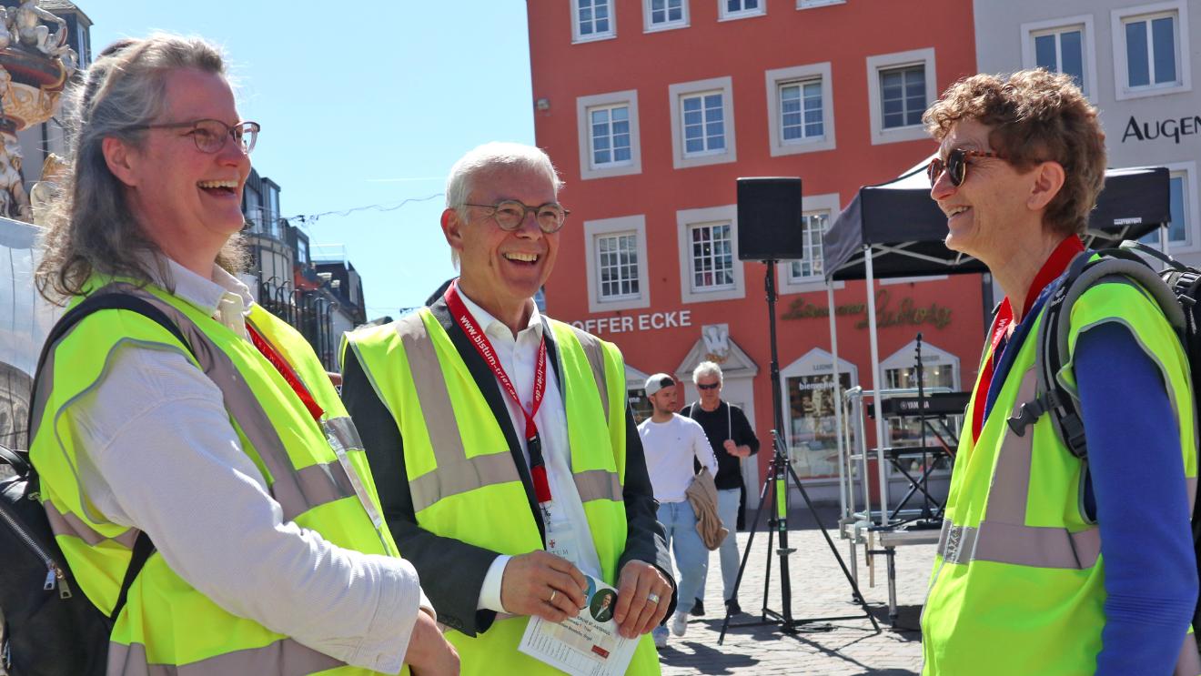 Zwei Frauen und ein Mann mit Warnwesten stehen auf dem Hauptmarkt und lachen sich an
