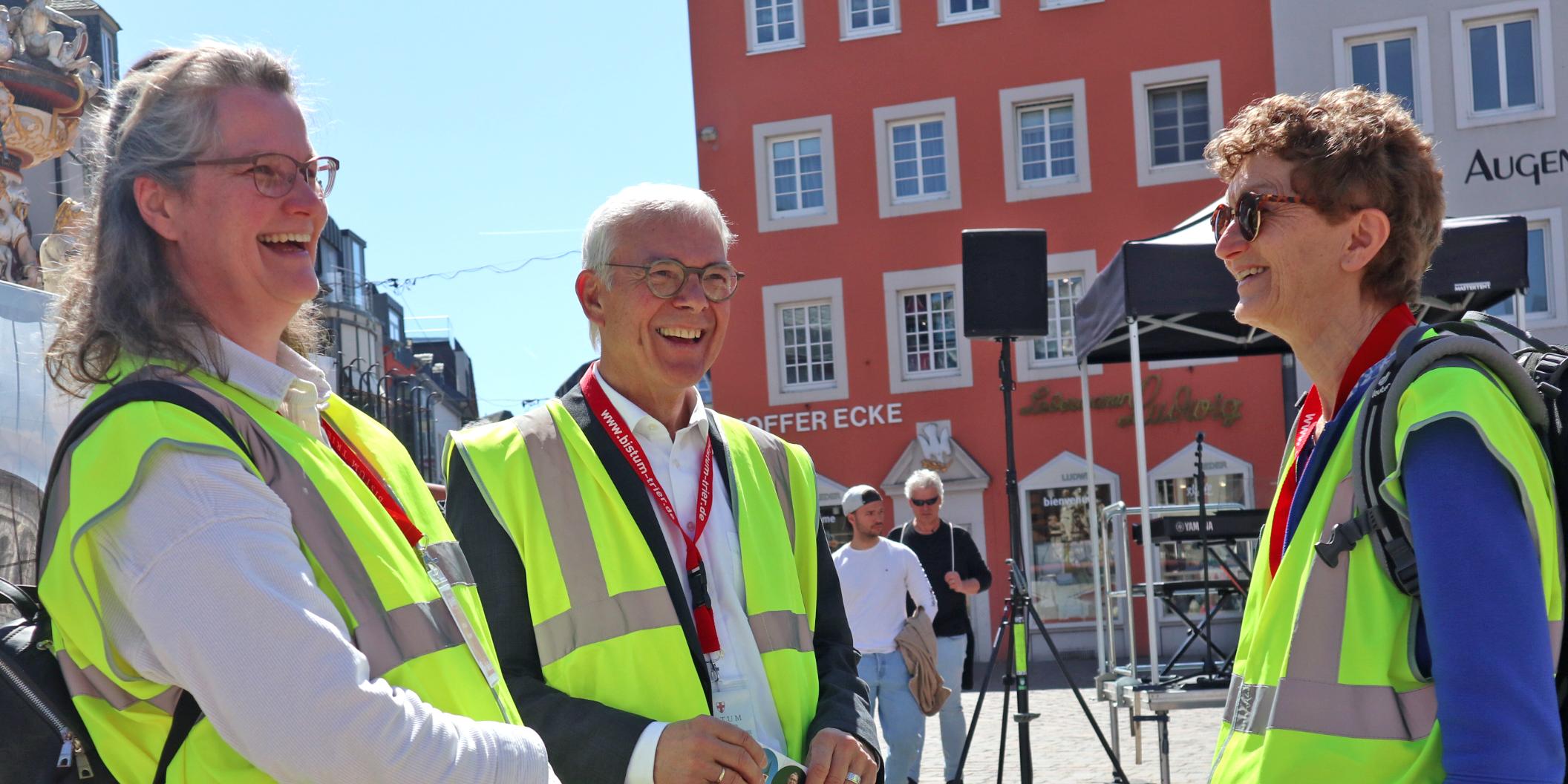 Zwei Frauen und ein Mann mit Warnwesten stehen auf dem Hauptmarkt und lachen sich an