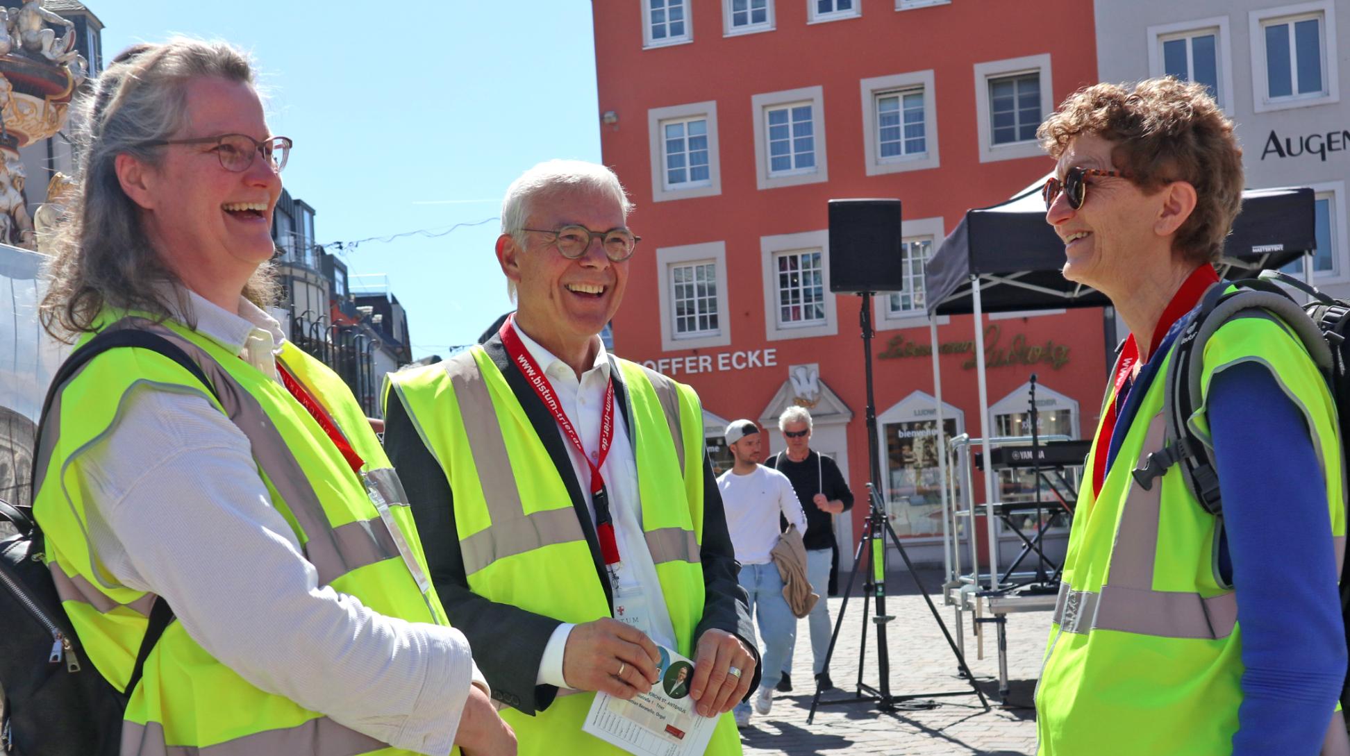 Zwei Frauen und ein Mann mit Warnwesten stehen auf dem Hauptmarkt und lachen sich an
