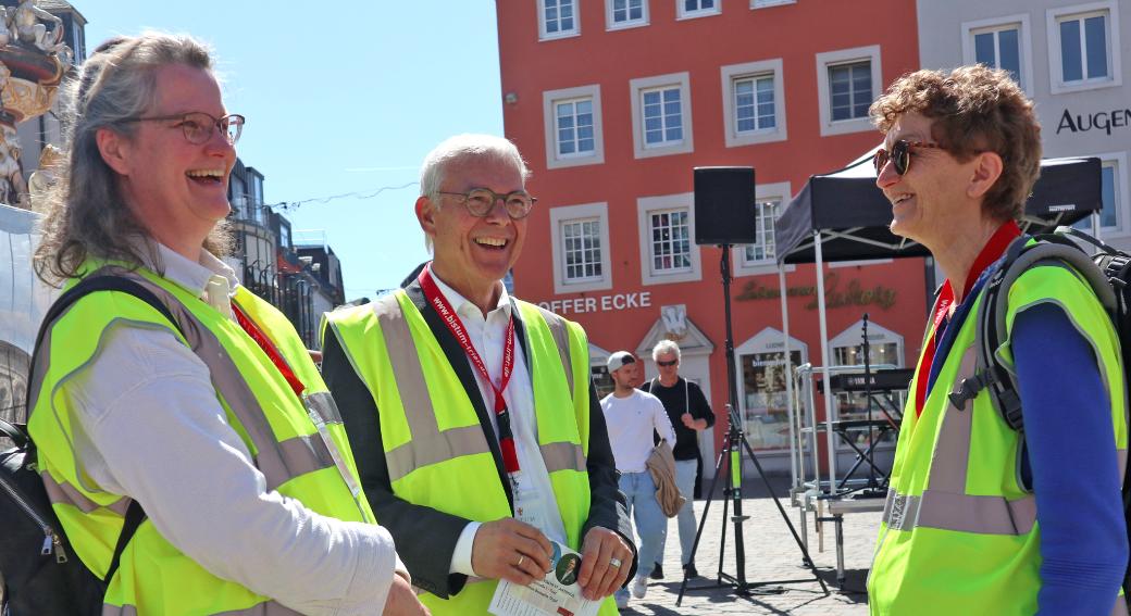 Zwei Frauen und ein Mann mit Warnwesten stehen auf dem Hauptmarkt und lachen sich an
