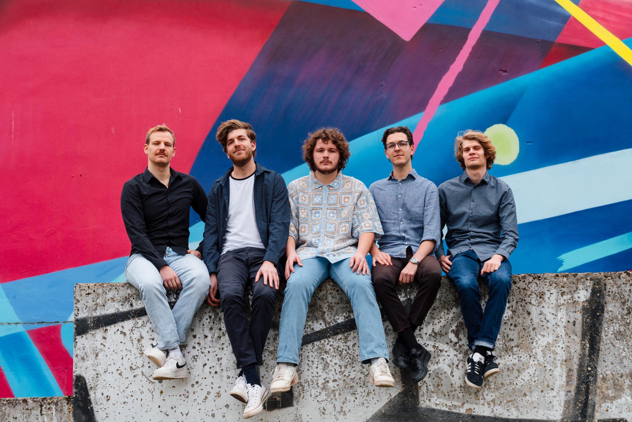 Die Band Rough Mix sitzt auf einer Mauer vor eine großen Graphity