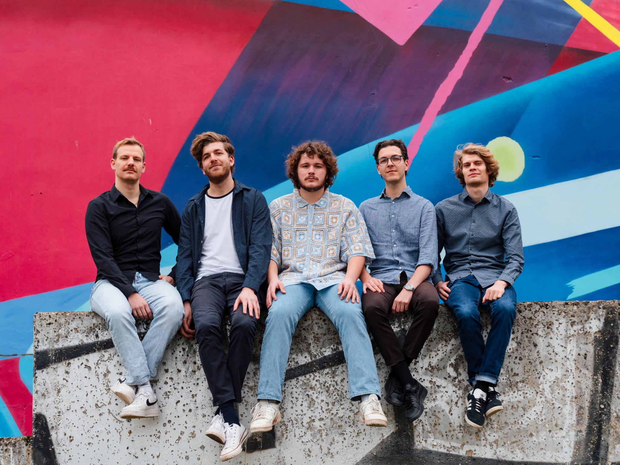 Die Band Rough Mix sitzt auf einer Mauer vor eine großen Graphity