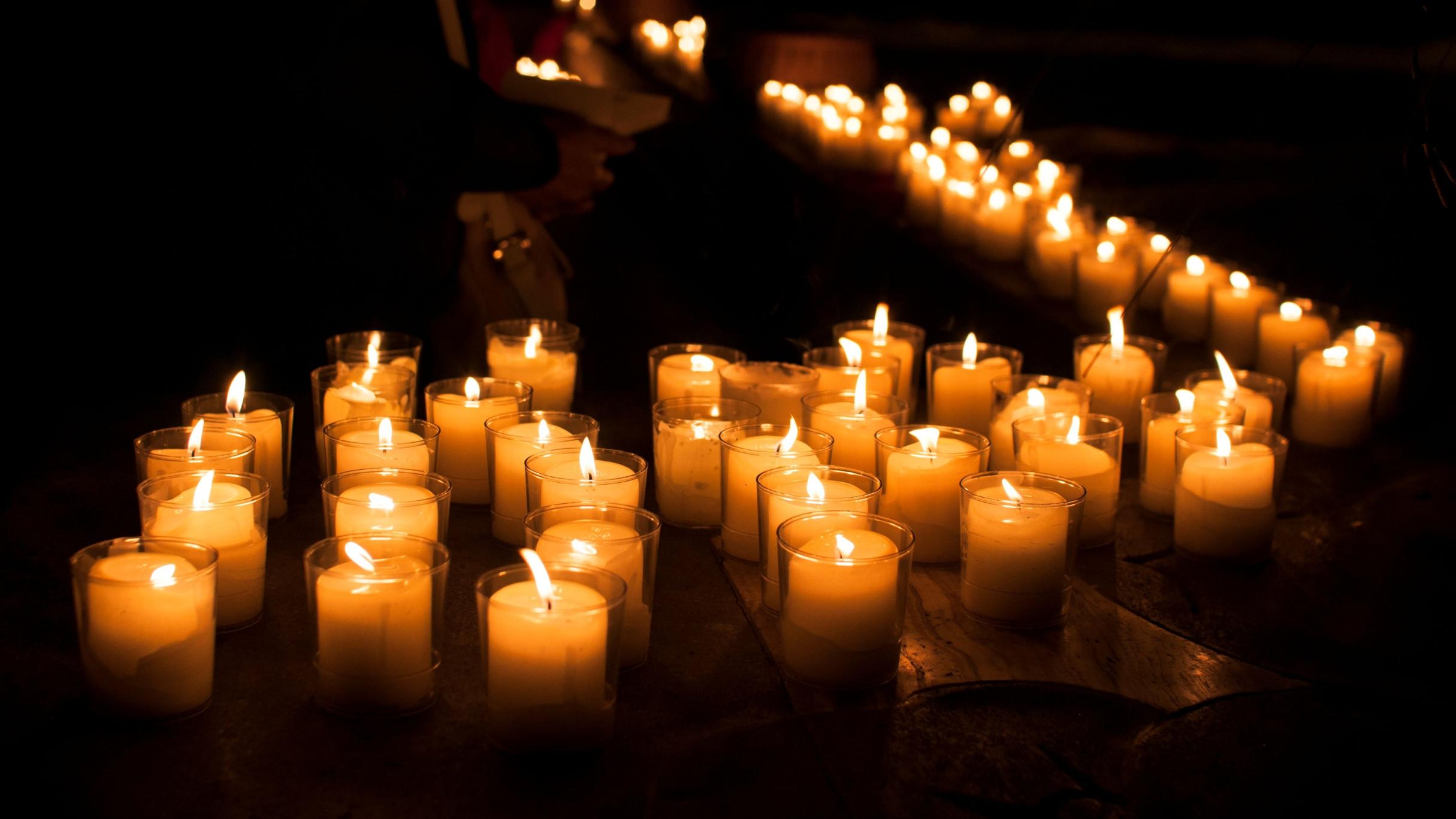 Vor einem dunklen Hintergrund stehen viele brennende Kerzen (c) Julia Fröder Vor einem dunklen Hintergrund stehen viele brennende Kerzen