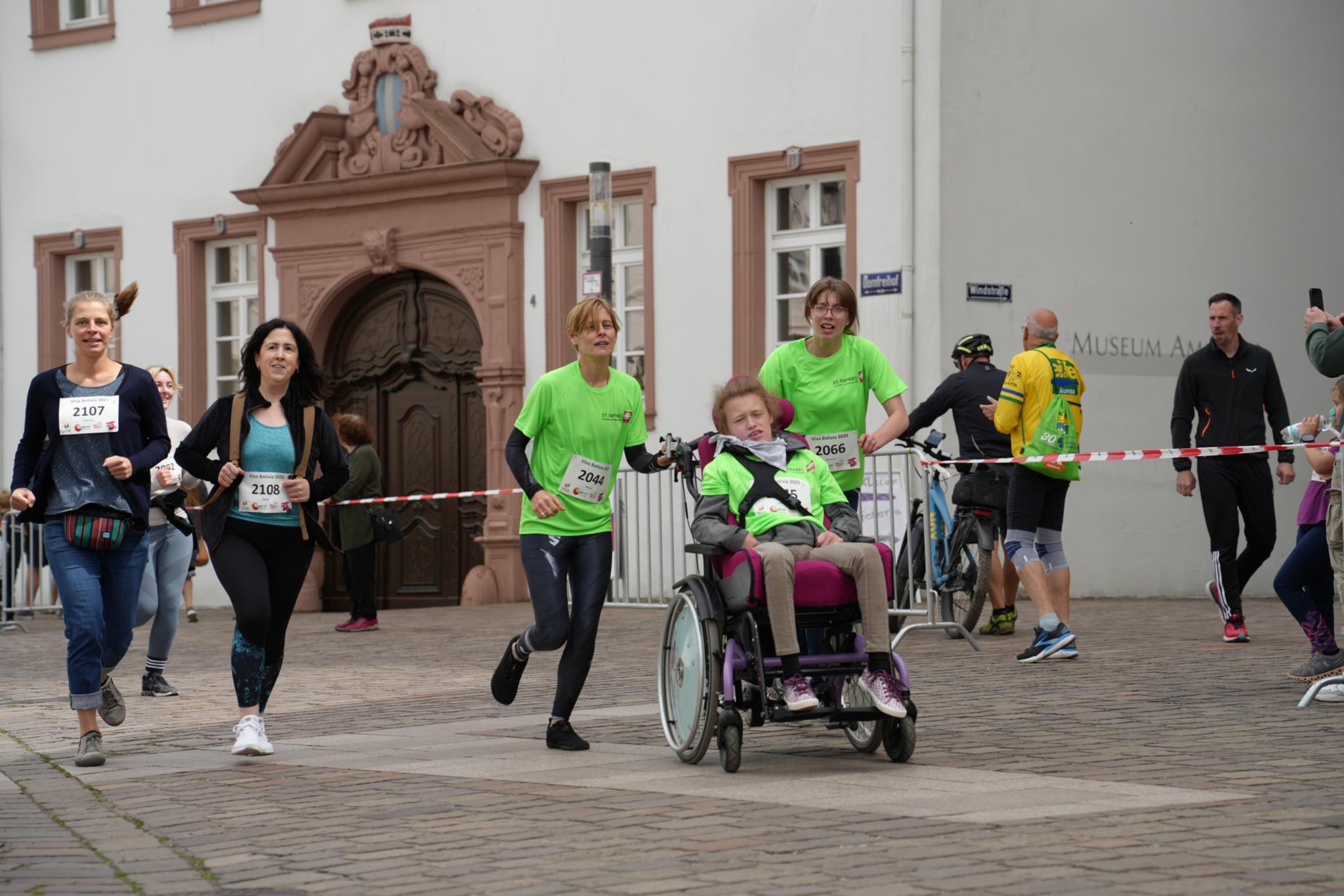 Fünf Menschen, davon eine Person im Rollstuhl, laufen über die Strecke
