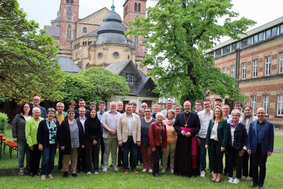 Eine Gruppe von Menschen steht zusammen mit Bischof Ackermann auf einer Wiese. Im Hintergrund ist der Dom