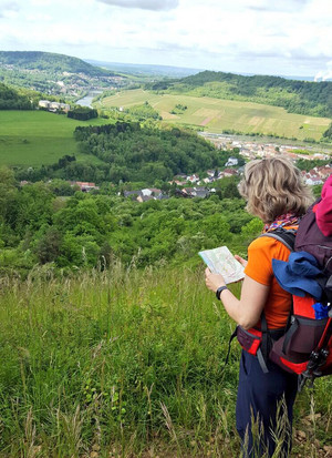 Eine Frau mit Rucksack und Wanderstöcken schaut auf eine Landkarte